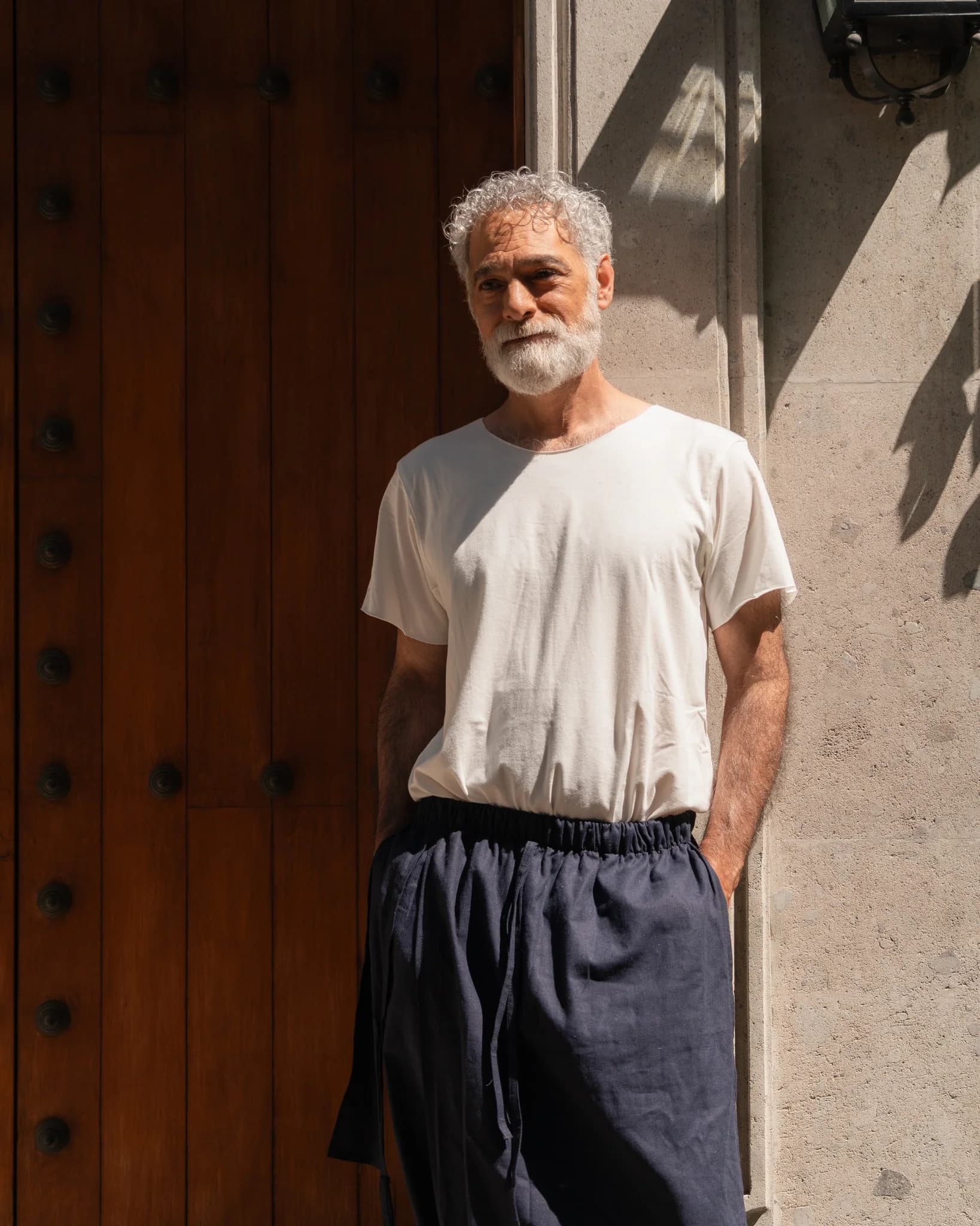 Hombre con camiseta de algodón y pantalón de lino frente a una puerta de madera