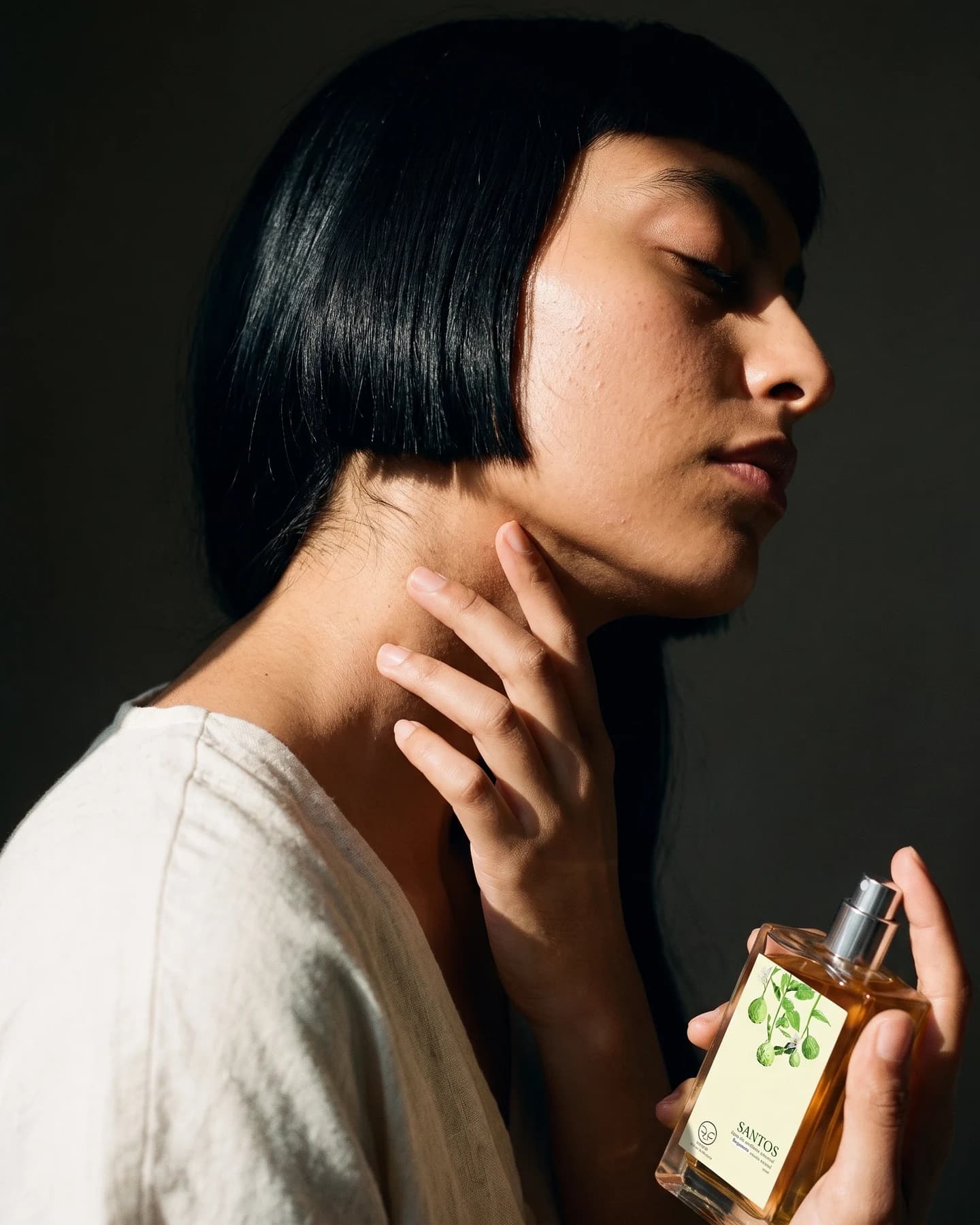 Una mujer se lleva los dedos al cuello, donde acaba de ponerse el perfume, con el frasco todavía en la otra mano