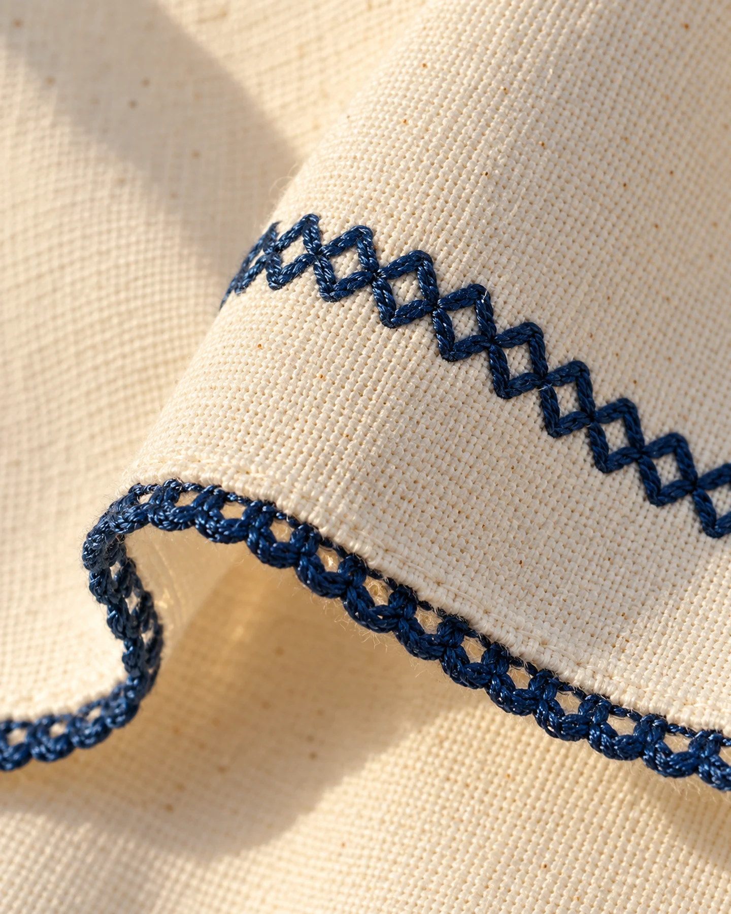 Poncho Cannes en crudo con bordado azul, en macro, la textura del material